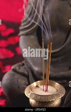 Buddha mit Räucherstäbchen unter Blütenblättern, Detail Stockfoto