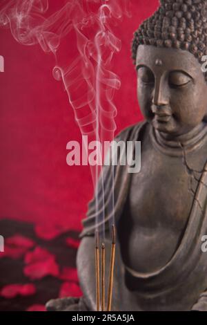 Buddha mit Räucherstäbchen unter Blütenblättern Stockfoto
