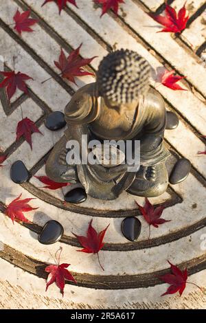 buddha, der auf dem Symbol des Lebens sitzt, in den Händen ein Steinbrief mit ZEN Stockfoto