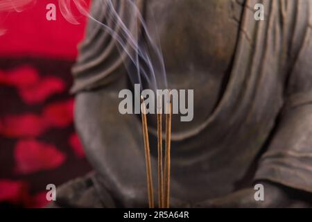 Buddha mit Räucherstäbchen unter Blütenblättern, Detail Stockfoto