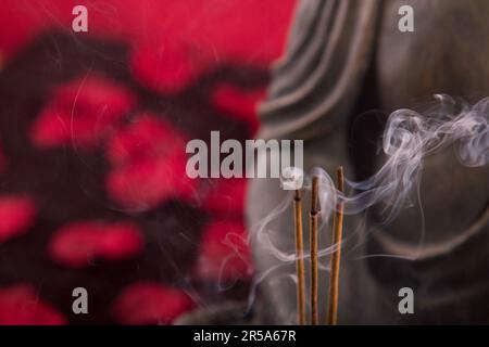 Buddha mit Räucherstäbchen unter Blütenblättern, Detail Stockfoto