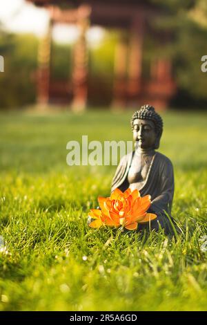 buddha mit orangefarbener Lotos-Blume auf einer Wiese in einem chinesischen Garten Stockfoto