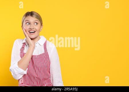 Wunderschöne junge Frau in einer sauberen gestreiften Schürze auf orangefarbenem Hintergrund. Platz für Text Stockfoto