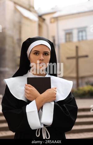 Junge Nonne mit Bibel in der Nähe von Gebäuden im Freien Stockfoto