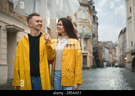 Reizendes junges Paar mit Regenschirm, das unter Regen auf der Straße der Stadt spaziert Stockfoto