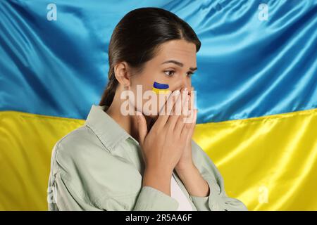 Traurige junge Frau mit gefalteten Händen nahe der ukrainischen Flagge Stockfoto