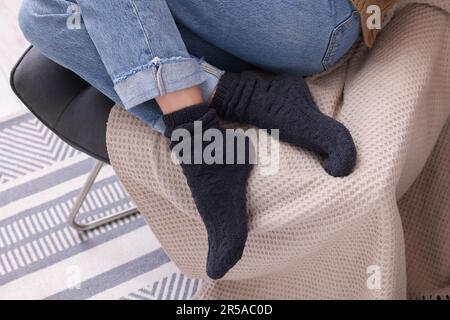 Eine Frau in warmen Socken, die zu Hause auf einem Sessel sitzt, schließt Stockfoto