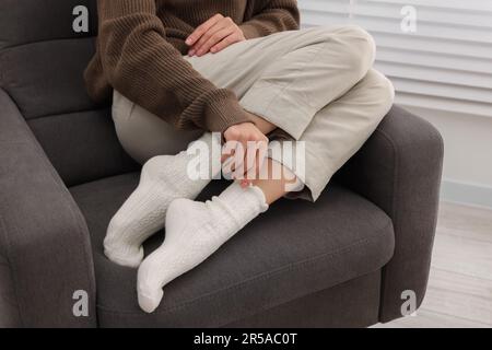 Eine Frau in warmen Socken, die sich zu Hause auf dem Sessel entspannt Stockfoto