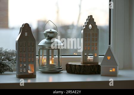 Wunderschöne Kerzenhalter in Hausform und Weihnachtsdekor auf Fensterbank im Innenbereich Stockfoto