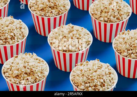 Rot-weiß gestreifte Eimer voller Popcorn. Pappschachteln gefüllt mit salzigen und köstlichen Snacks aus frisch geöffnetem Mais. Pakete werden verteilt in Stockfoto