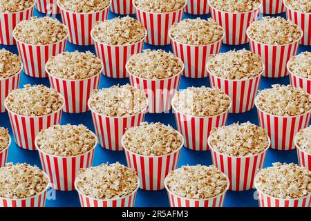 Rot-weiß gestreifte Eimer voller Popcorn. Pappschachteln gefüllt mit salzigen und köstlichen Snacks aus frisch geöffnetem Mais. Pakete werden verteilt in Stockfoto