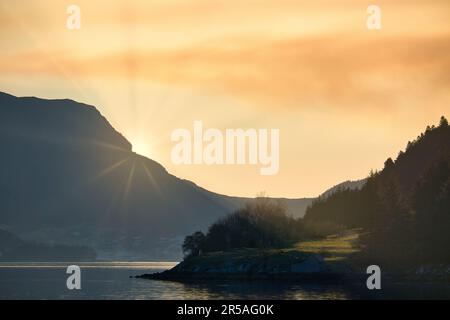 Fjord mit Blick auf Berge und Fjordlandschaft in Norwegen. Die Sonne geht hinter dem Berg unter. Landschaftsaufnahmen aus dem Norden Skandinaviens Stockfoto
