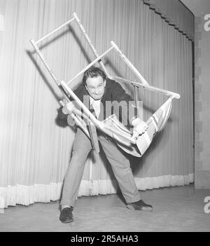 Carl-Gustaf Lindstedt, 1921-1992, hier in Verbindung mit einer Revue in den 1950er, wo er in einem klassischen Sketch versucht, einen Liegestuhl richtig zusammenzustellen. Sieht nicht so aus, als ob er Erfolg hat. Die Konstruktion des Stuhls, in seiner Einfachheit und Genialität, ist ein Rätsel. Schweden 1953. Kristoffersson Ref. BK100-4 Stockfoto