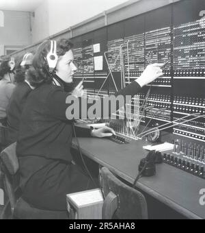 Telefonie in den 1950er. Frauen, die in einer Telefonzentrale arbeiten, als Telefonisten. Ein manuell betriebenes Telefonkommunikationssystem, bei dem die eingehenden Anrufe vom Betreiber weitergeleitet und an eine andere Telefonnummer umgeleitet wurden, in diesem Fall lokal innerhalb des Gebäudes, das ein Unternehmen oder eine Organisation mit vielen internen Telefonleitungen bedient. Die Telefonzentrale konnte Nachrichten entgegennehmen und Sie in die Warteschleife setzen, wenn die Leitung besetzt war. Schweden 1953. Kristoffersson Ref. BM99-4 Stockfoto