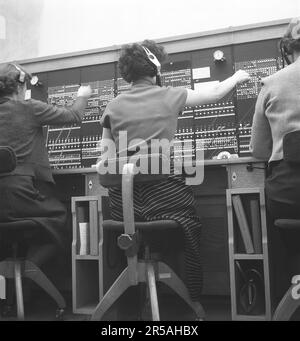 Telefonie in den 1950er. Frauen, die in einer Telefonzentrale arbeiten, als Telefonisten. Ein manuell betriebenes Telefonkommunikationssystem, bei dem die eingehenden Anrufe vom Betreiber weitergeleitet und an eine andere Telefonnummer umgeleitet wurden, in diesem Fall lokal innerhalb des Gebäudes, das ein Unternehmen oder eine Organisation mit vielen internen Telefonleitungen bedient. Die Telefonzentrale konnte Nachrichten entgegennehmen und Sie in die Warteschleife setzen, wenn die Leitung besetzt war. Schweden 1953. Kristoffersson Ref. BM99-10 Stockfoto