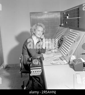 Telefonie in den 1950er. Eine Frau, die an einer Telefonzentrale arbeitet, als Vermittlung. Ein manuell betriebenes Telefonkommunikationssystem, bei dem die eingehenden Anrufe vom Betreiber weitergeleitet und an eine andere Telefonnummer umgeleitet wurden, in diesem Fall lokal innerhalb des Gebäudes, das ein Unternehmen, Hotel oder eine Organisation mit vielen internen Telefonleitungen bedient. Die Telefonzentrale konnte Nachrichten entgegennehmen und Sie in die Warteschleife setzen, wenn die Leitung besetzt war. Sie ist eine Mitarbeiterin von hotell Malmen in Stockholm und verbindet die ein- und ausgehenden Anrufe der Hotelgäste. Schweden 1953. Stockfoto