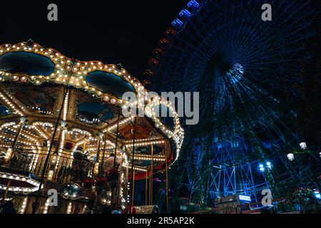 Nachts wird ein farbenfrohes Karussell beleuchtet, und im Hintergrund ist ein Riesenrad zu sehen Stockfoto