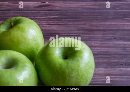 Drei frische grüne Äpfel auf einem Holztisch vor rustikalem Holzhintergrund, perfekt zur Veranschaulichung eines gesunden Lebensstils Stockfoto