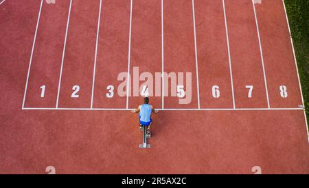 Kaukasischer männlicher Sprintläufer allein auf der Sportstrecke, nimmt Startposition ein und läuft in Reihe vier, Luftlinie über Schuss. Stockfoto