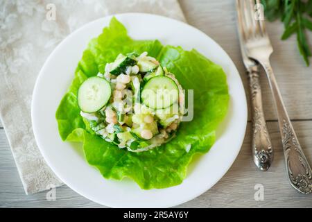 Frischer Sommersalat mit Bohnen, Reis, Gurken und anderem Gemüse auf einem Teller auf einem Holztisch. Stockfoto