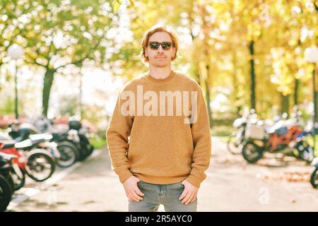 Herbstporträt im Freien eines gutaussehenden jungen Mannes mit braunem, flauschigem Fleece-Pullover und Sonnenbrille Stockfoto