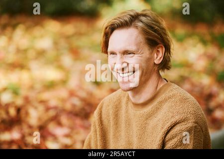 Nahaufnahme des hübschen, lachenden, rothaarigen Mannes, der einen beigen, flauschigen Fleece-Pullover trägt Stockfoto