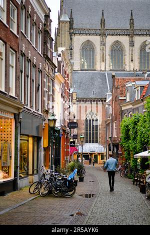 Haarlem, Holland, 23. Mai 2022: Alleinstehender Mann, der allein die Warmoesstraat-Einkaufsstraße in Haarlem hinuntergeht. Die Grote Kerk Kirche im Hintergrund. Stockfoto