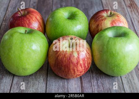 Vier reife Äpfel in einer Reihe auf einer Holztischfläche, verzehrfertig Stockfoto
