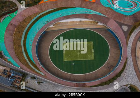 Dieses Stockfoto zeigt einen Tennisplatz in einem runden Gebäude, umgeben von farbenfrohen Sitzgelegenheiten Stockfoto