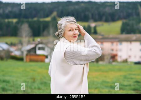 Außenporträt einer schönen Frau mittleren Alters, die einen weißen Mantel trägt Stockfoto