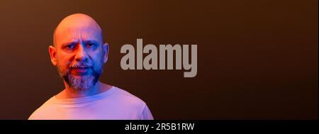 Kahlköpfiger Mann mit Bart, ernsthaft, der verdächtig in die Kamera schaut. Aufmerksam und fokussiert. Isoliert auf dunkelrotem Hintergrund. Stockfoto