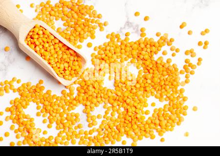Rote Linsen in einem Holzlöffel und auf einer weißen Marmortheke mit Kopierbereich Stockfoto