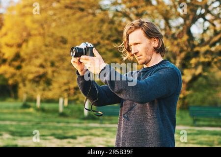 Außenporträt eines gutaussehenden jungen Mannes, der mit einer alten alten alten Filmkamera Fotos im grünen, sonnigen Park macht Stockfoto