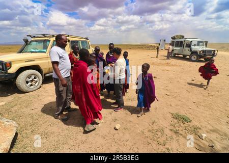 30. Dezember 2017, Serengeti National Park, Tansania-A Tourist teilt ihre Snacks und hilft den Maasai-Kindern mit Wasser und Geld Stockfoto