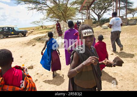 30. Dezember 2017, Serengeti-Nationalpark, Tansania-A Young Maasai moran Junge und andere Maasai Kinder nähern sich Touristen am Serengeti Tor Stockfoto