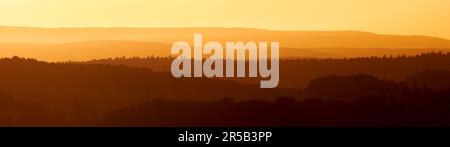 Ein faszinierender Blick auf den orangefarbenen Sonnenuntergang über den silhouettierten Hügeln Stockfoto