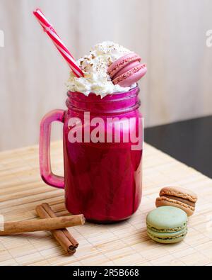 Ein Glas pinkfarbenes Getränk mit Eis und zwei rote Getränke im Hintergrund, mit Zimt auf der Oberseite Stockfoto