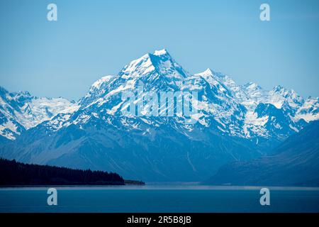Ein malerischer Blick auf eine majestätische Bergkette, die über ein großes Gewässer ragt, umgeben von üppigen grünen Bäumen und Bergen Stockfoto