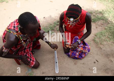 Die Mitglieder des Maasai mara-Stammes machen Feuer mit einem trockenen Gras und einem traditionellen 406mm mm flachen Büffelmesser von masai mara, um die Brandauslösungsmethode zu demonstrieren Stockfoto