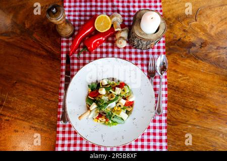 Ein Blick von oben auf eine Schüssel mit mediterranem Salat mit Kräutern, Gemüse und Olivenöl auf dem Tisch Stockfoto