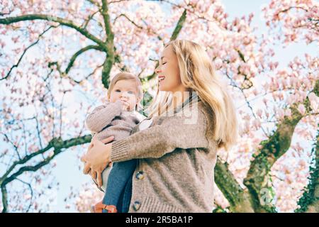 Außenporträt einer glücklichen jungen Mutter mit einem niedlichen Mädchen unter einem blühenden Frühlingsbaum, Blick von unten Stockfoto