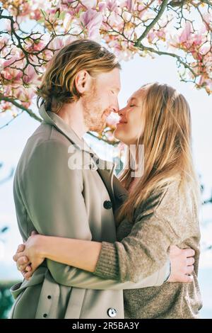 Glückliches romantisches Paar, das sich unter einem blühenden Baum küsst Stockfoto