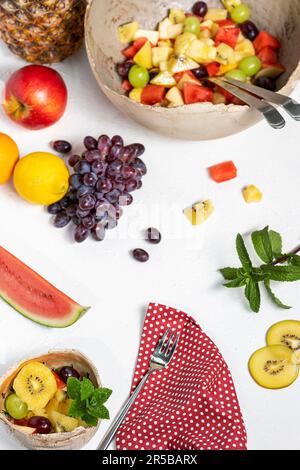 Frisch zubereiteter Obstsalat in einer großen, klassischen Schüssel und einer gefüllten Dessertschüssel. Mit Obst und Minze dekoriert. Stockfoto