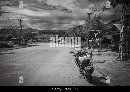 Ein großes Motorrad, das in der Nähe eines blauen Straßenschilds auf der Straße QL40 geparkt ist, das auf die Grenze zu Kambodscha und Laos in der Gemeinde Bo Y, dem Viertel Ngoc Hoi, im Cent zeigt Stockfoto