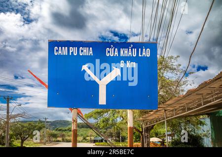 Ein blaues Straßenschild, das auf die Grenze zwischen Kambodscha und Laos in der Gemeinde Bo Y, Bezirk Ngoc Hoi, im zentralen Hochland in Vietnam zeigt. Das Schild ist lokalisiert Stockfoto