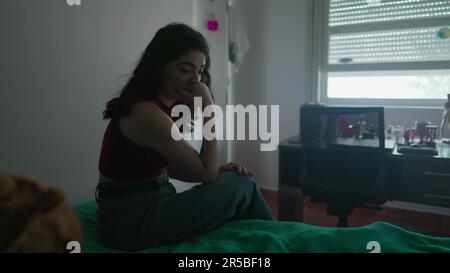 Eine nachdenkliche junge Frau sitzt am Bett mit nachdenklichem Ausdruck. Weibliche Person in 30s mit inneren Emotionen Stockfoto