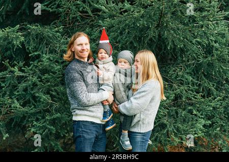 Außenporträt einer wunderschönen, glücklichen, jungen Familie mit 4 Personen, die im Pinienwald posiert, warme Pullover trägt, ein Paar mit einem kleinen Jungen und einem kleinen Mädchen, das gut ist Stockfoto