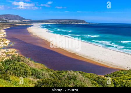 Foto von Noordhoek Beach in der Nähe von Kapstadt vom Chapmans Peak Drive in blauem Himmel mit einer Sandbank zwischen dem Meer und braunem Flusswasser, fotografiert in S Stockfoto