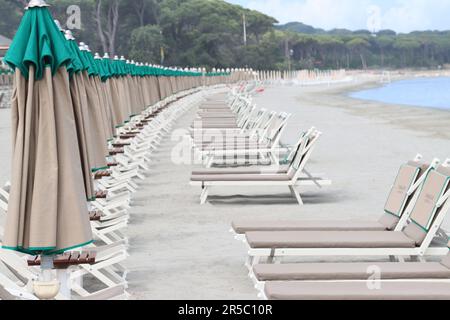 Eine Reihe von Stühlen und Sonnenschirmen liegen am Strand entlang Stockfoto