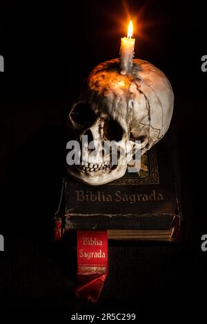 Eine glühende Kerze wird auf einen Stapel Bücher gestellt, der auf einem menschlichen Schädel ruht Stockfoto